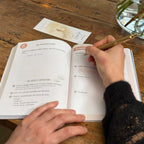 Carnet + marque-page sur table, personne qui écrit dans le carnet, lifestyle ambiance douce